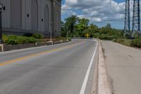 a picture of an empty street that is by some buildings in the distance with trees and bushes in front