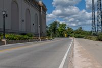 a picture of an empty street that is by some buildings in the distance with trees and bushes in front