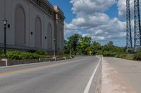 a picture of an empty street that is by some buildings in the distance with trees and bushes in front