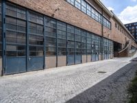 a sidewalk and brick sidewalk in front of large windows on a brick building on the corner of a cobblestone road