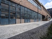 a sidewalk and brick sidewalk in front of large windows on a brick building on the corner of a cobblestone road