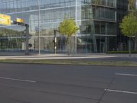 the empty street is lined with green grass and trees along side the building as well as a glass wall