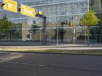 the empty street is lined with green grass and trees along side the building as well as a glass wall