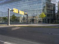 the empty street is lined with green grass and trees along side the building as well as a glass wall