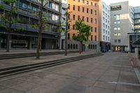 the empty street and some buildings in a city in summer time as pedestrians pass by