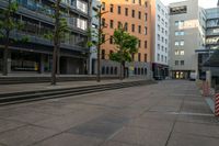 the empty street and some buildings in a city in summer time as pedestrians pass by
