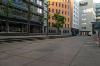 the empty street and some buildings in a city in summer time as pedestrians pass by