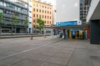 an empty city street with many buildings and trees in the background, including two stores at the corner