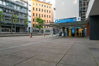 an empty city street with many buildings and trees in the background, including two stores at the corner