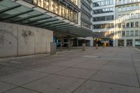 people on the sidewalk in an empty public area with concrete barriers and windows on the opposite side