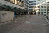 people on the sidewalk in an empty public area with concrete barriers and windows on the opposite side