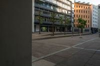 a view of buildings from an open square on a sidewalk in the city with two people walking by