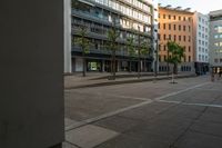 a view of buildings from an open square on a sidewalk in the city with two people walking by