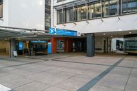 an empty parking lot near a large building, on which is an entrance with a bus stop and benches