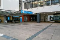 an empty parking lot near a large building, on which is an entrance with a bus stop and benches