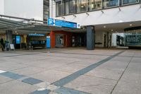 an empty parking lot near a large building, on which is an entrance with a bus stop and benches