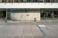 an empty bus stop with a bicycle parked next to it near a wall and windows