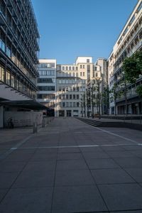 the empty concrete courtyard of a large building with lots of windows and a white car