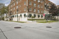 an empty street with two buildings and trees behind it in front of the road and on the right corner there is a stop sign and traffic light