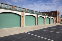 a row of green garage doors on a building with red brick walls and green shutters