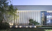 an exterior photograph of a modern house with trees in front of it in the evening