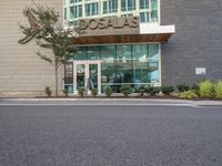 the parking lot in front of the building has signage and a building with a tree