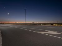 a city street filled with traffic at night time and lights on poles above it is a empty runway