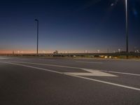 a city street filled with traffic at night time and lights on poles above it is a empty runway