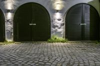 a stone and brick wall with black double doors and a lamp fixture in the middle