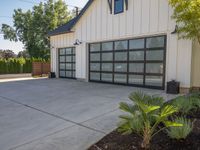 a garage that has two black garage doors and plants on the front walk way of it