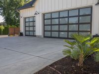 a garage that has two black garage doors and plants on the front walk way of it