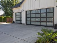 a garage that has two black garage doors and plants on the front walk way of it