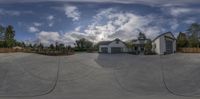 a house in a driveway with a garage and lots of trees behind it with a cloudy sky above