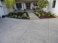 a patio with small tree on it and walkway in front of house and a porch to right