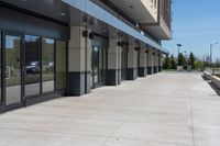 a building with two rows of glass doors, outside and on side of walkway and pavement