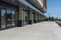 a building with two rows of glass doors, outside and on side of walkway and pavement