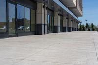 a building with two rows of glass doors, outside and on side of walkway and pavement