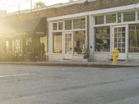 a yellow fire hydrant on the side of the road with the sun shining in front of a store front