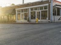 a yellow fire hydrant on the side of the road with the sun shining in front of a store front