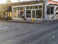 a yellow fire hydrant on the side of the road with the sun shining in front of a store front