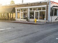 a yellow fire hydrant on the side of the road with the sun shining in front of a store front