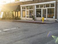 a yellow fire hydrant on the side of the road with the sun shining in front of a store front