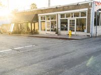 a yellow fire hydrant on the side of the road with the sun shining in front of a store front