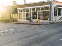 a yellow fire hydrant on the side of the road with the sun shining in front of a store front