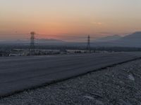 a person riding a motorcycle down the middle of the road with power lines overhead at sunset