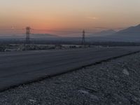 a person riding a motorcycle down the middle of the road with power lines overhead at sunset