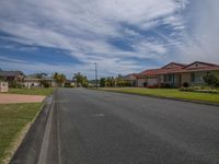 the view of an empty residential street in a suburban area with a few houses and trees