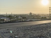 a deserted road in the daytime and a factory near it at sunset in the background