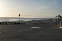 an empty road near a beach and waves as well as cars on the sand and houses on the beach