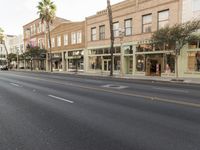 empty street with shops and cars lining the sidewalk in an urban area with palm trees